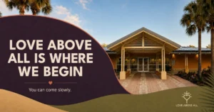 Front entrance of a modern church framed by palm trees beneath the words, “Love Above All Is Where We Begin,” with the invitation, “You can come slowly.”